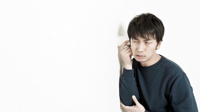 壁に耳を当てて隣の様子をうかがう男性の写真