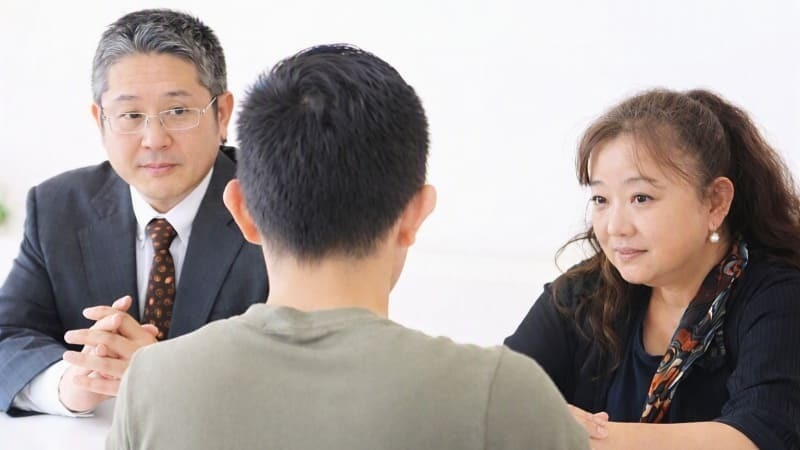 創業1997年・相談実績10万件以上の探偵事務所で、加藤なぎさ代表と加藤正明主任が依頼者と向き合い、長年の調査経験を基に最適な浮気調査や人探しの方法を丁寧に提案している面談シーン。白い背景の会議室で、スーツ姿の男性とスカーフを着用した女性が依頼者と対話し、信頼と実績に基づく専門的な相談体制を示す画像。